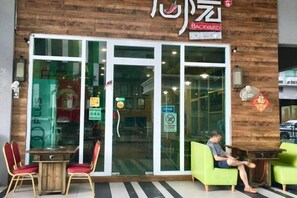 Un restaurant doté d’une façade en bois, de grandes fenêtres et d’une terrasse avec des chaises rouges.