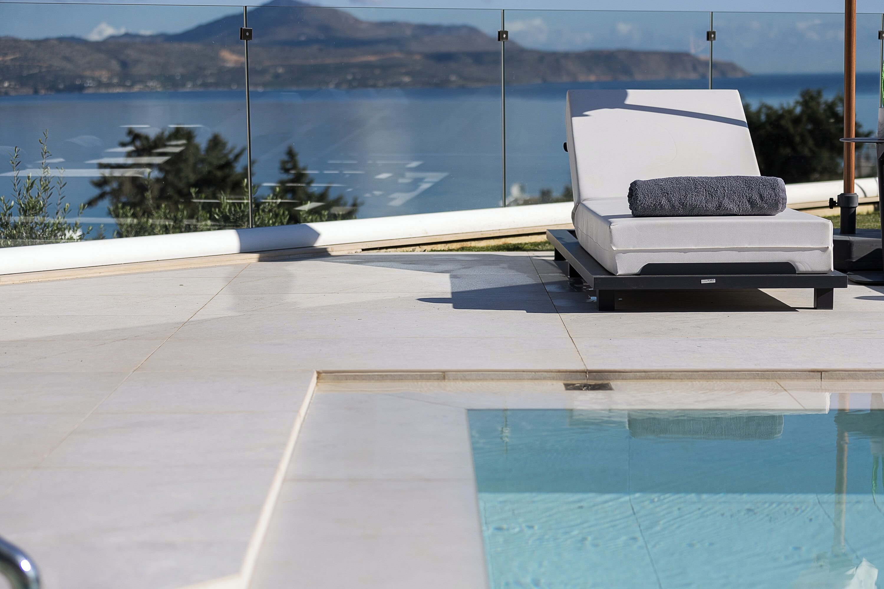 A poolside area with a lounge chair and a towel, overlooking a body of water and distant mountains.