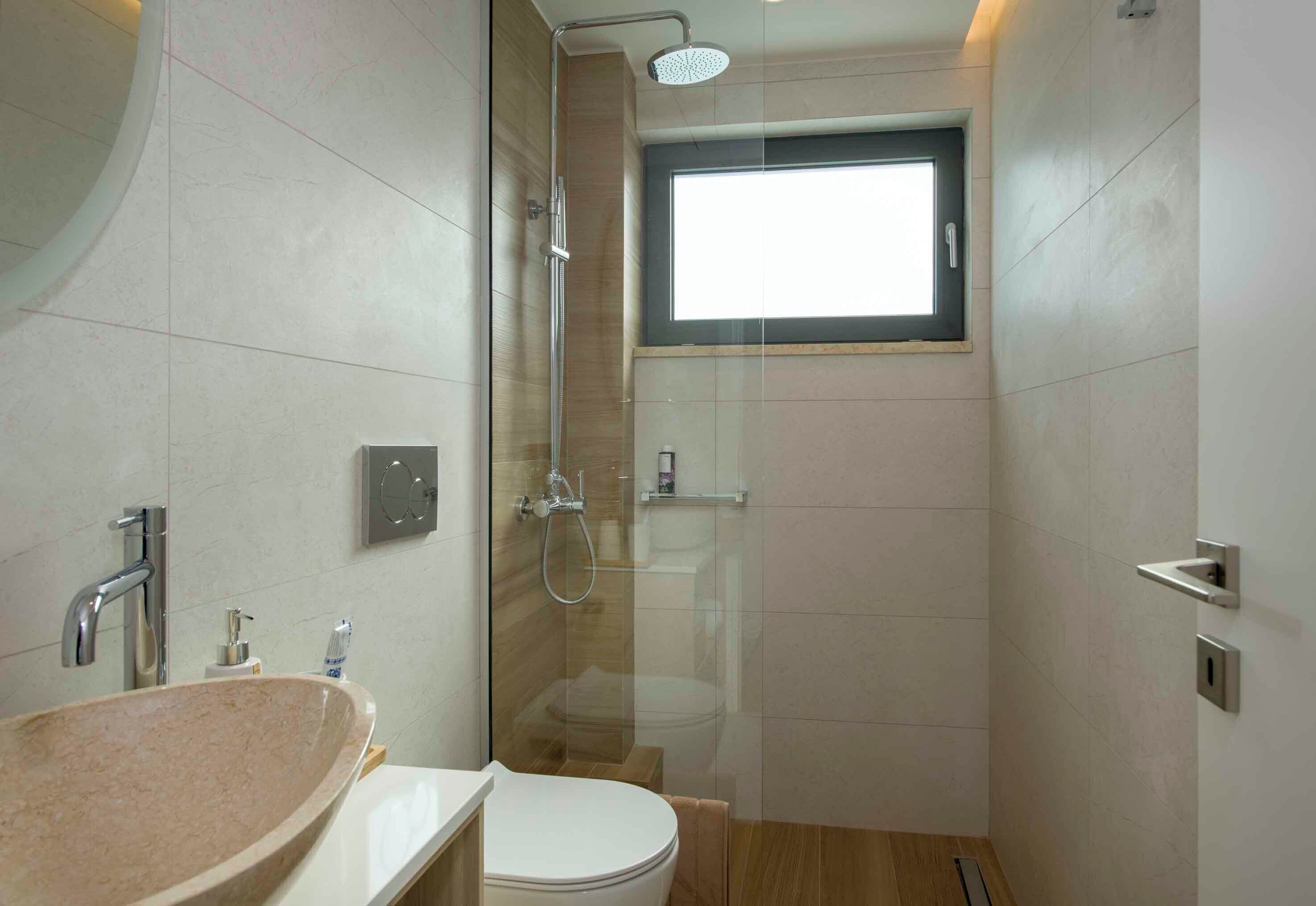 A modern bathroom with a glass-enclosed shower, a sink with a beige countertop, and a toilet.