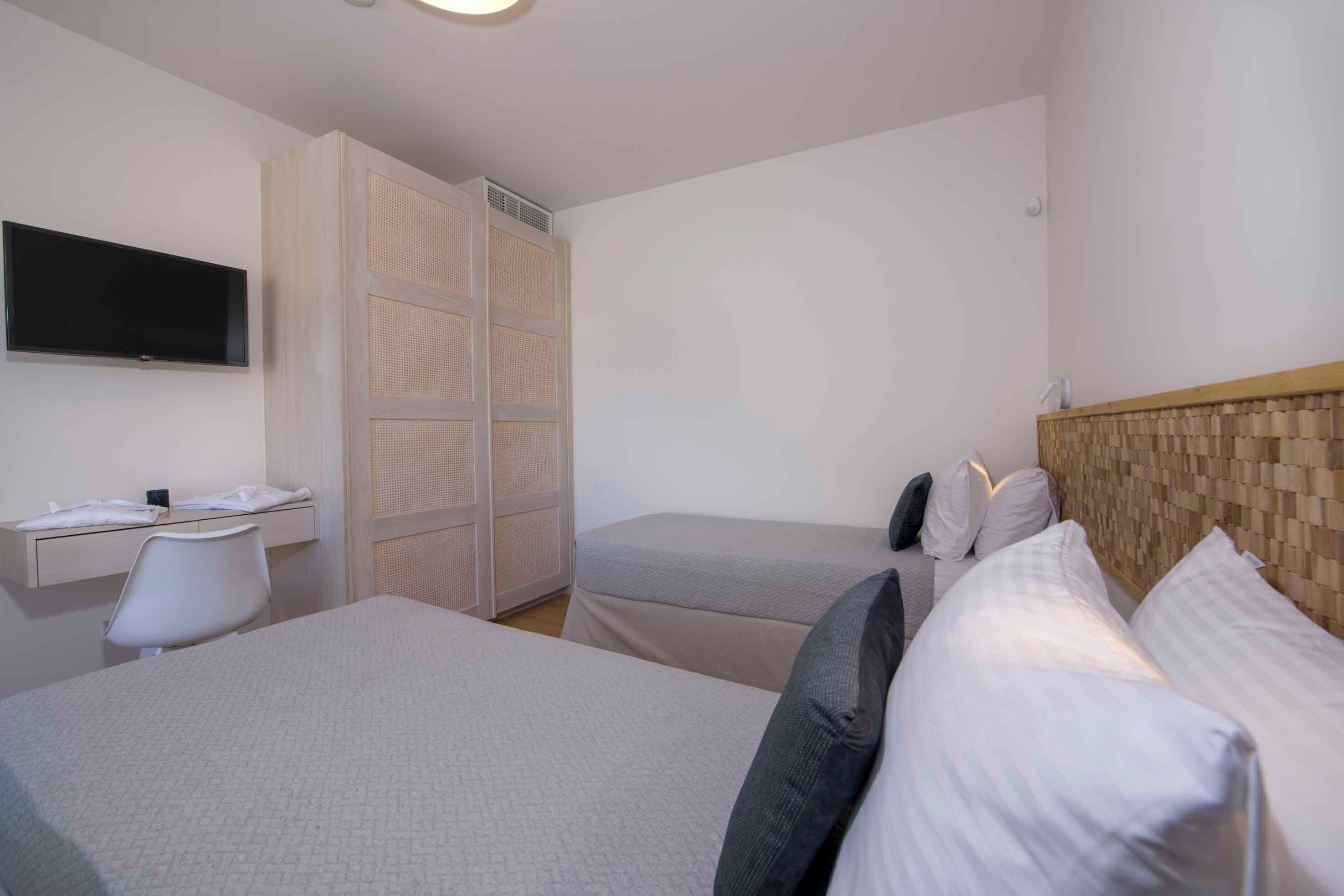 Een hotelkamer met twee bedden, een bureau met een televisie en een kledingkast.