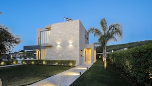 A modern house with a stone facade, solar panels, and a well-maintained garden with a pathway leading to the entrance. - Kalyves Royal Villa (Apokoronas)