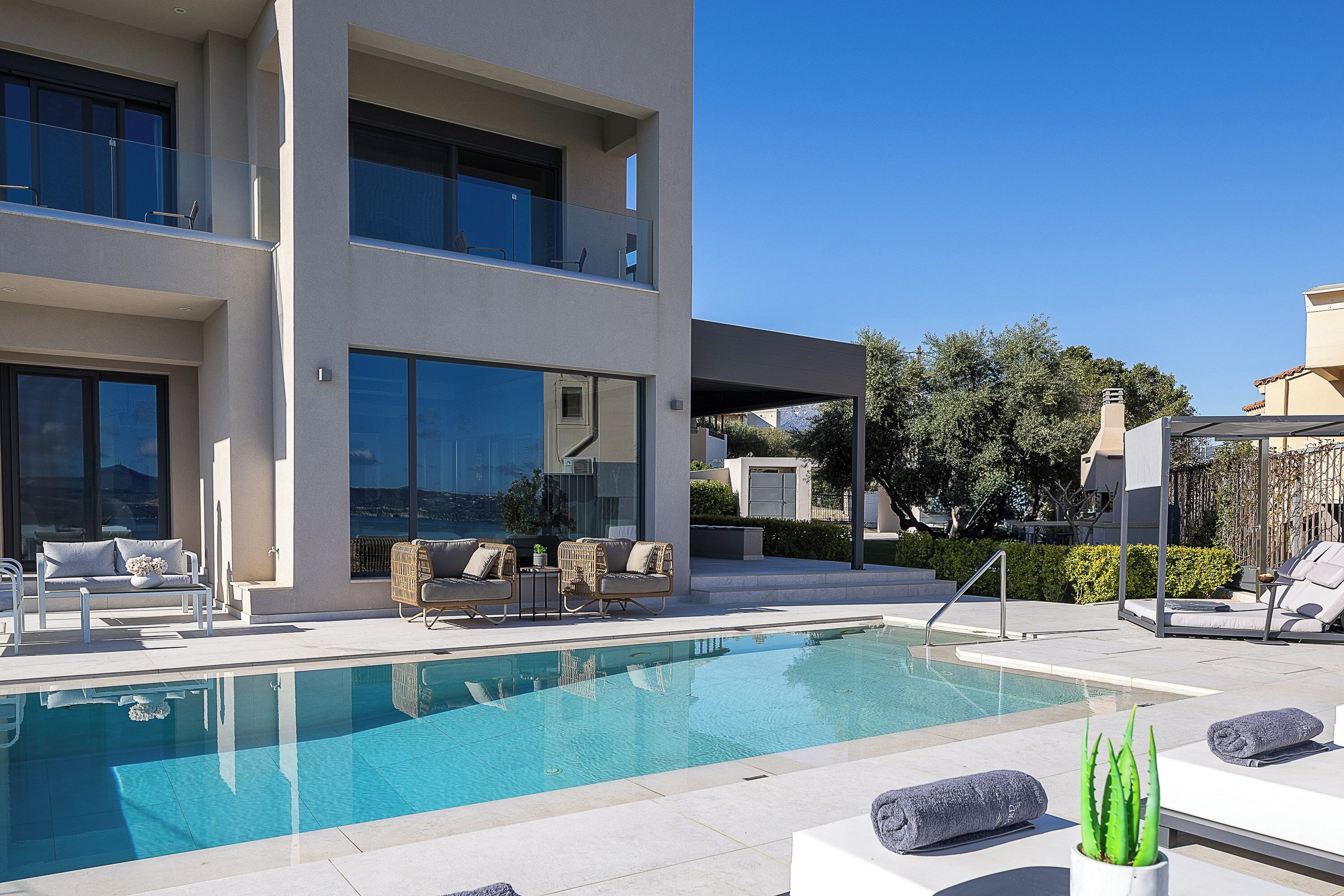 A modern pool area with a clear pool, lounge chairs, and a two-story building with large windows.