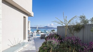 A modern outdoor pool area with lounge chairs and a view of the sea. - Kalyves Royal Villa (Apokoronas)