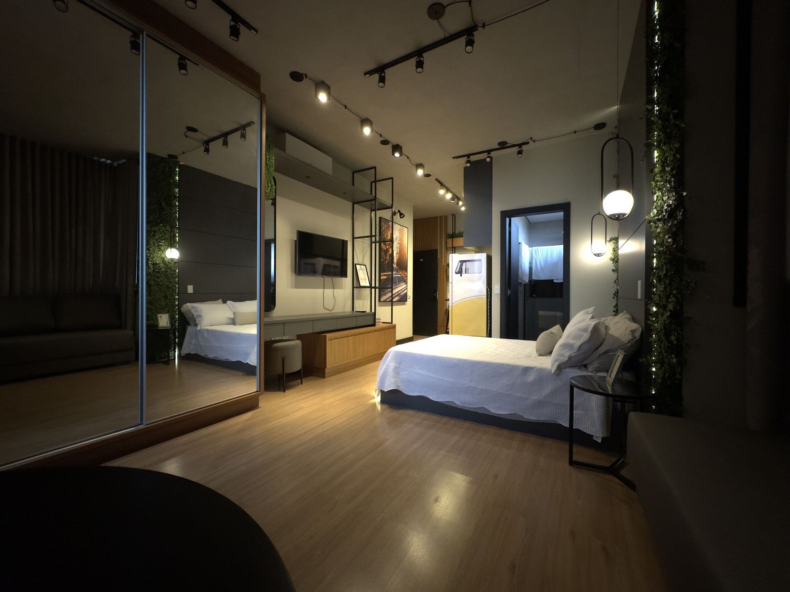 Ein modernes Schlafzimmer mit einem großen Spiegel, einem Bett, einem Schreibtisch und einem Fernseher.