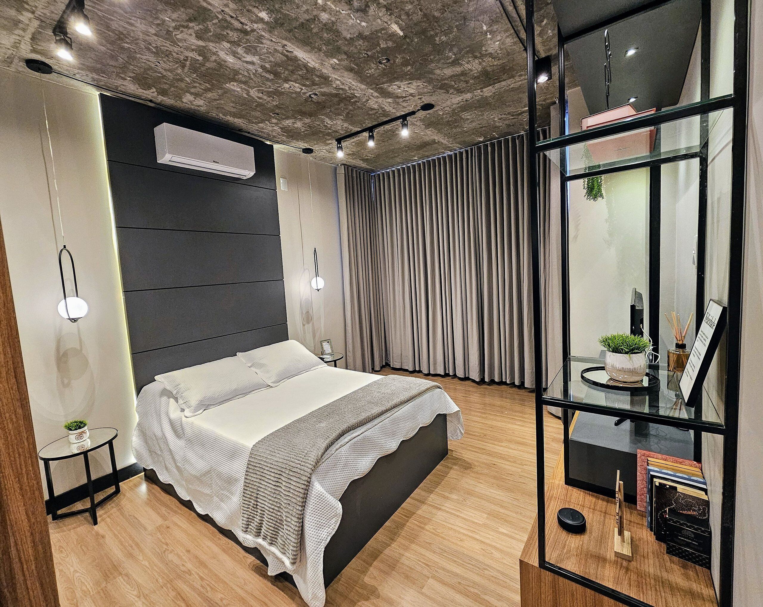 Ein modernes Schlafzimmer mit einem großen Bett, einem kleinen Nachttisch, einer Wand-Klimaanlage und einer Glastrennwand mit Pflanze und Schild.