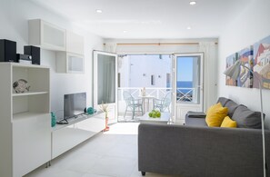 Un soggiorno moderno con un divano grigio, una TV e un balcone con vista sul mare.