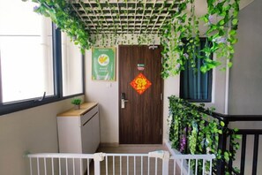 A staircase with a white railing, a wooden door with a red decoration, and green plants hanging from the ceiling. - Forest Ants Homestay in Forest City (Gelang Patah)