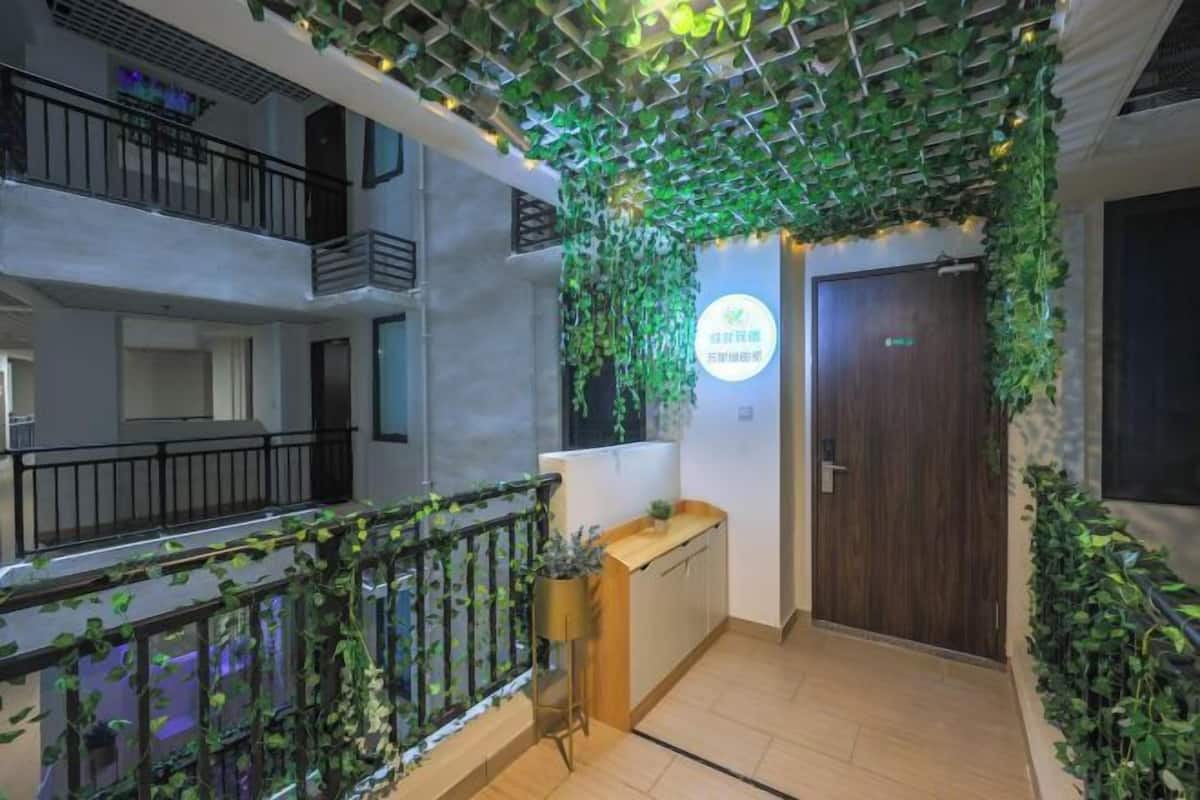 Un hall d’hôtel avec un comptoir d’accueil en bois, une porte en bois sombre, et des plantes vertes sur les murs et au plafond.