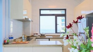 A modern kitchen with a large window, a countertop with kitchenware, and a view of the sea.