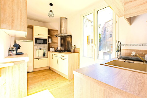 A modern kitchen with wooden cabinets, stainless steel appliances, and a large window offering a view of the street.