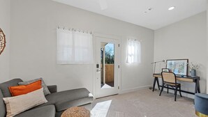 A modern living room with a grey sofa, a desk with a chair, and a door leading outside. - Comfortable walk to Magnolia & Just a short drive to Baylor (Waco)
