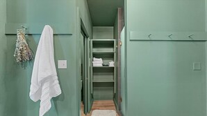 A hallway with a green wall, a white towel hanging on the left, and a closet with shelves containing folded towels. - Comfortable walk to Magnolia & Just a short drive to Baylor (Waco)