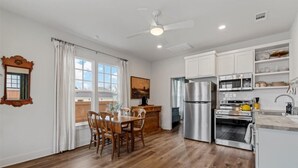 A modern kitchen with white cabinets, stainless steel appliances, and a dining area with wooden chairs and a table. - Comfortable walk to Magnolia & Just a short drive to Baylor (Waco)