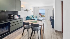 A modern kitchen with a dining area, a sofa, and a view of the sea.