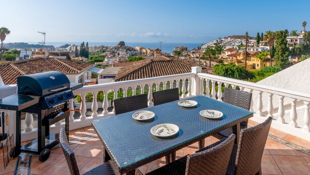 Una terrazza con tavolo e sedie, un barbecue e vista su una località costiera.