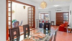 Un'ampia sala da pranzo con tavolo e sedie in vetro, una porta in legno e vista su un patio esterno da una porta aperta.