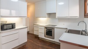 Una cucina moderna con mobili bianchi, forno integrato, microonde e lavello.