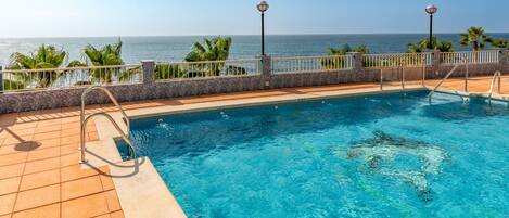A swimming pool with a view of the ocean, surrounded by palm trees and a tiled deck.