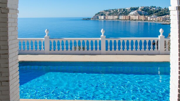 Piscina com vista clara para o mar e uma encosta ao fundo.