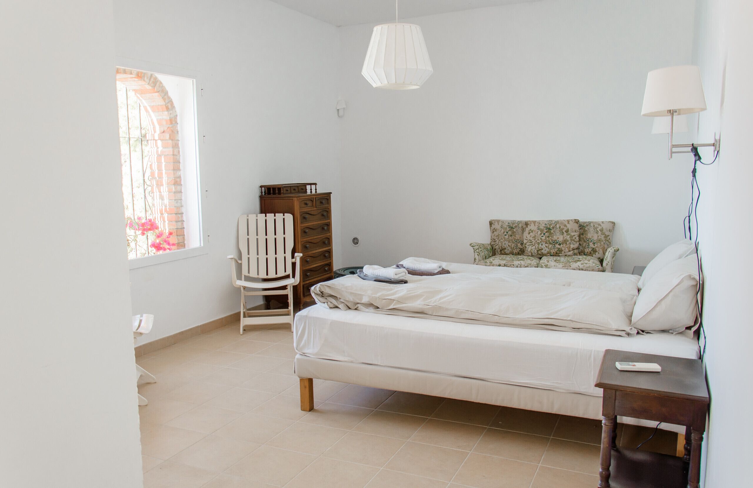 Una camera da letto con un letto, una cassettiera, una sedia e una finestra vista fiori.