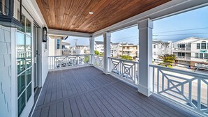 A covered porch with a wooden ceiling, white railings, and a view of neighboring houses. - Rooftop Deck & Ocean Views—Luxury 5BR/4.5BA  Single Family, Across from Beach! (Ocean City)