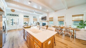 A spacious kitchen with a large island, wooden cabinets, and a dining area with wicker chairs. - Rooftop Deck & Ocean Views—Luxury 5BR/4.5BA  Single Family, Across from Beach! (Ocean City)