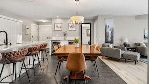 A modern kitchen with a central island, bar stools, and a dining table. - Water`s Edge | Pool | Hot Tub | Pets | Ground LVL (Invermere)