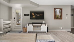 A modern living room with a flat-screen TV, a wooden coffee table, and a patterned rug. - Water`s Edge | Pool | Hot Tub | Pets | Ground LVL (Invermere)
