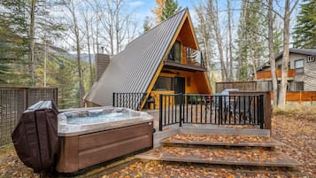 Une cabane avec un bain à remous, une terrasse en bois et une vue sur la forêt.