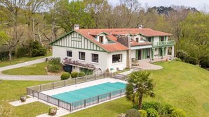 Ein zweigeschossiges Haus mit Swimmingpool, umgeben von einem gepflegten Rasen und Bäumen.