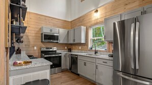 A modern kitchen with wooden paneling, stainless steel appliances, and a window providing a view of greenery.