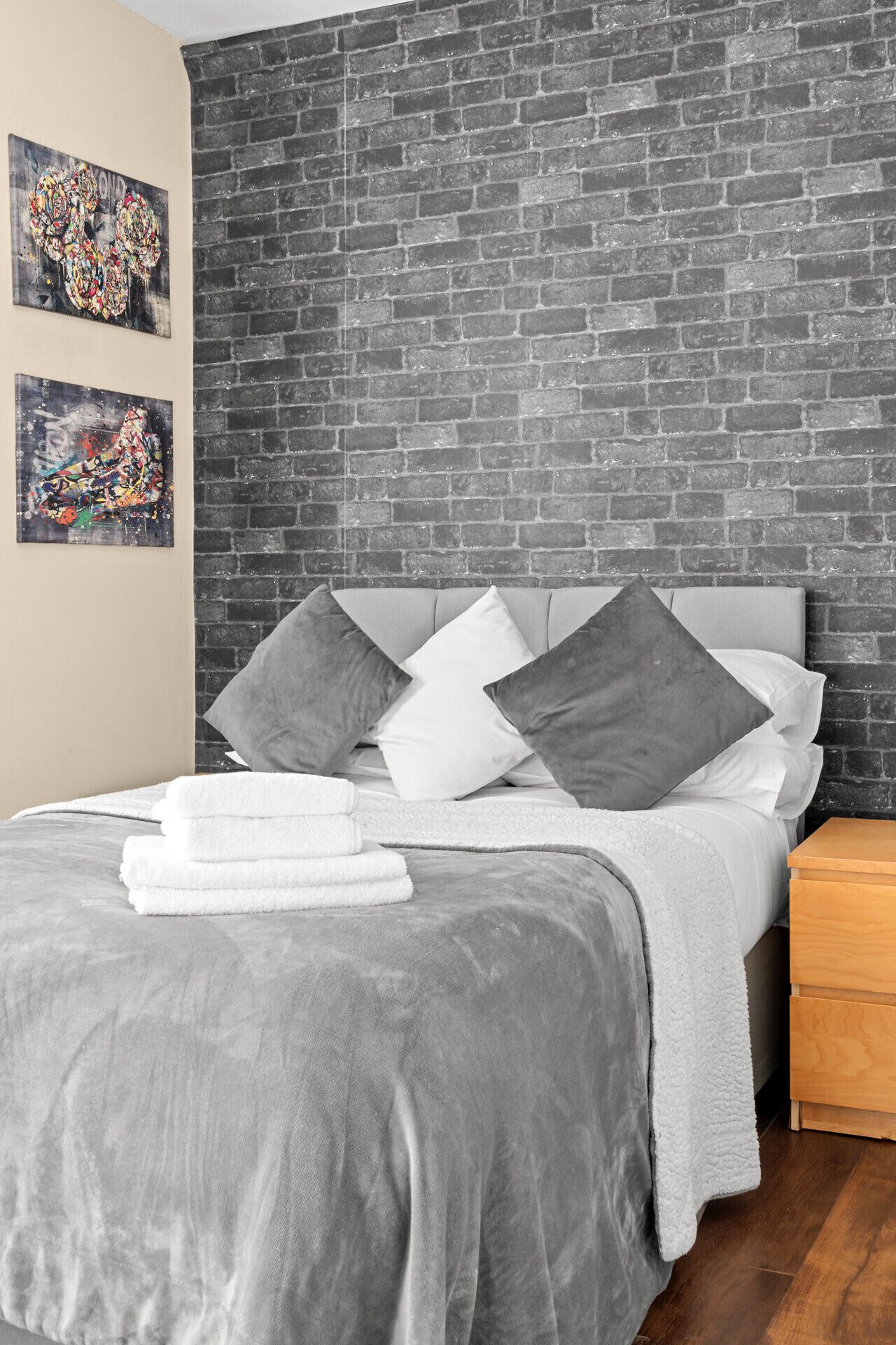 Une chambre à coucher moderne avec une tête de lit à motifs de briques, une couvre-lit grise et deux oreillers.
