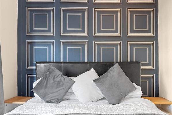 Ein Bett mit schwarzem Kopfteil, grauen und weißen Kissen und einer weißen Decke.