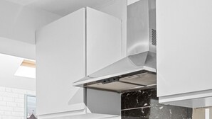 Una cocina moderna con armarios blancos, un salpicadero de mármol negro, una campana extractora de acero inoxidable y un horno empotrado.
