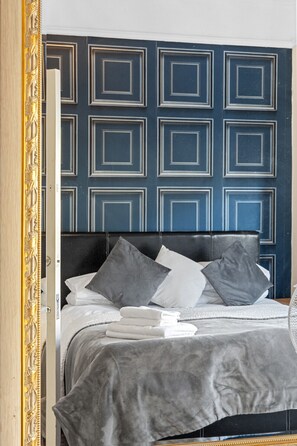 A bed with a dark headboard, grey and white pillows, and a grey blanket.