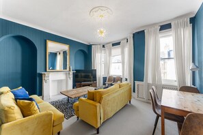 A living room with a sofa, armchair, TV, and a dining table.