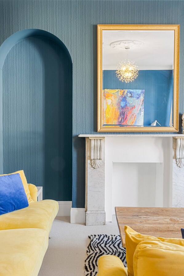 A room with a fireplace, a large mirror, and a yellow sofa.
