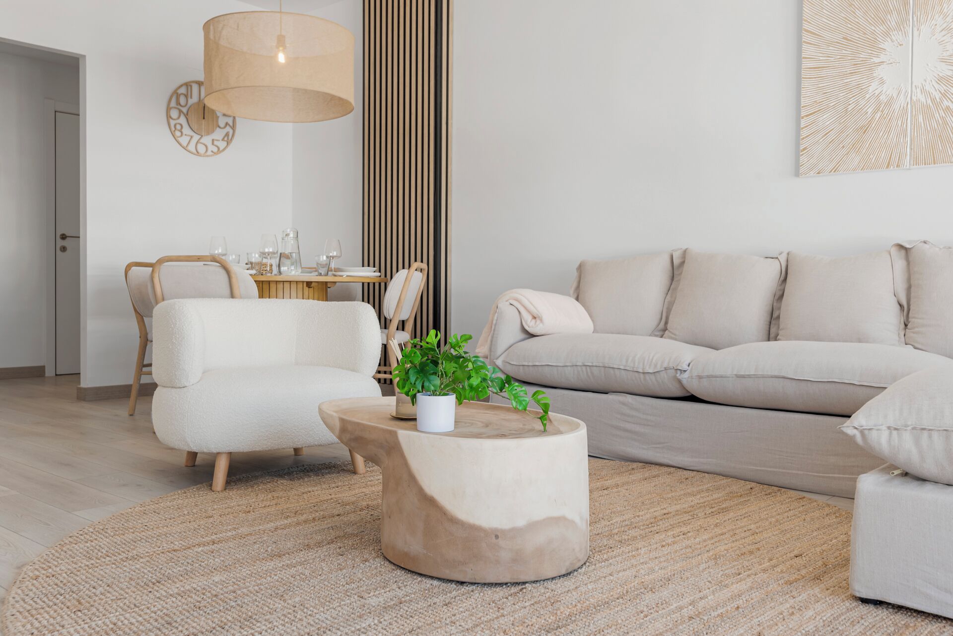 A modern living room with a beige sofa, a round coffee table, and a dining area with a wooden table and chairs.