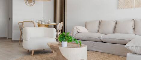 A modern living room with a beige sofa, a round coffee table, and a dining area with a wooden table and chairs.