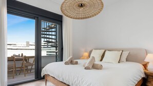 Ein Schlafzimmer mit einem großen Bett, einem Balkon mit Sitzgelegenheiten und Blick auf Gebäude.