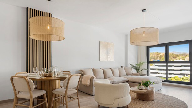 Ein modernes Wohnzimmer mit Essbereich, mit einem Holzesstisch, gedeckten Tellern und Gläsern, einem beigen Sofa und zwei runden Couchtischen.