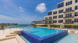 Un espace piscine avec une eau d’un bleu limpide, des marches menant à la piscine et un navire de croisière en arrière-plan.