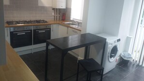 Una cocina compacta con estufa a gas, dos hornos, lavadora integrada y una pequeña mesa.