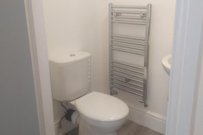 Un baño pequeño y blanco con inodoro, toallero y dispensador de papel higiénico.