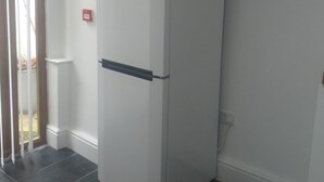 Una habitación de esquina con un refrigerador blanco, una puerta con picaporte y una ventana con persianas.