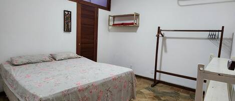 A bedroom with a bed, a ceiling fan, a wooden door, a wall-mounted shelf, and a drying rack.