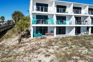 Un edificio de varios pisos con balcones, mobiliario exterior y una zona de playa arenosa.