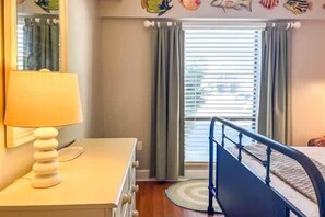 A bedroom with a bed, a dresser, a lamp, and a window with curtains.