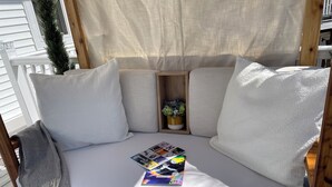 A wooden deck with a white cushioned bench, a small wooden shelf with a plant, and a magazine on the bench. - Serenity Haven: A Modern Retreat (Monroe)