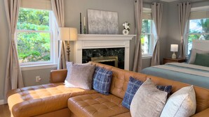 A cozy living room with a leather sofa, a fireplace, and a bed with a blue bedspread. - Serenity Haven: A Modern Retreat (Monroe)